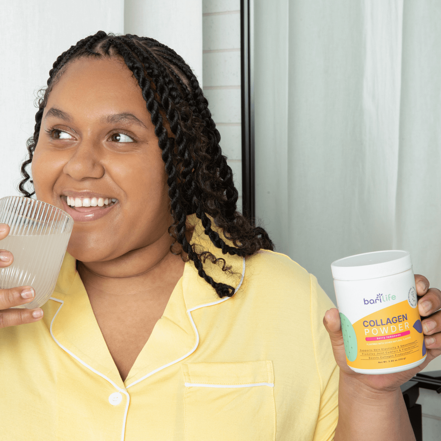 Smiling woman in yellow pajamas holding Bariatric Collagen Powder Berry Lemonade and a drink, promoting wellness.